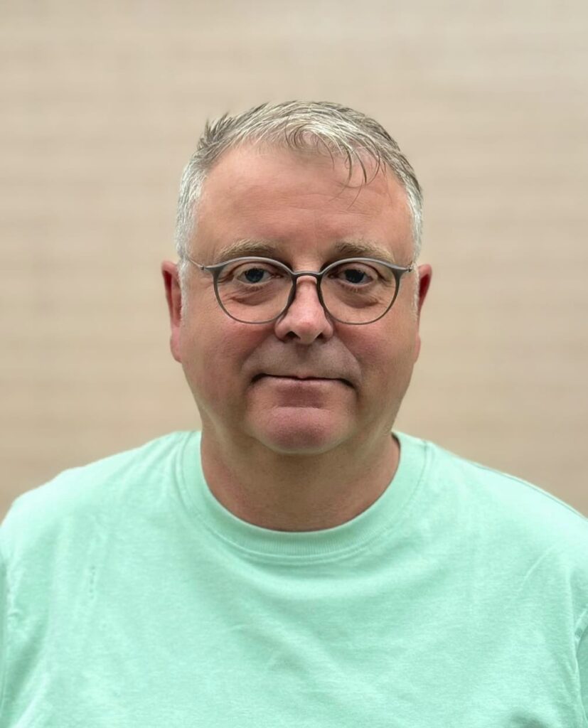 Mann mit ruhigem Ausdruck, Brille, grauem Haar, mintgrünem Hemd, neutrale Kulisse