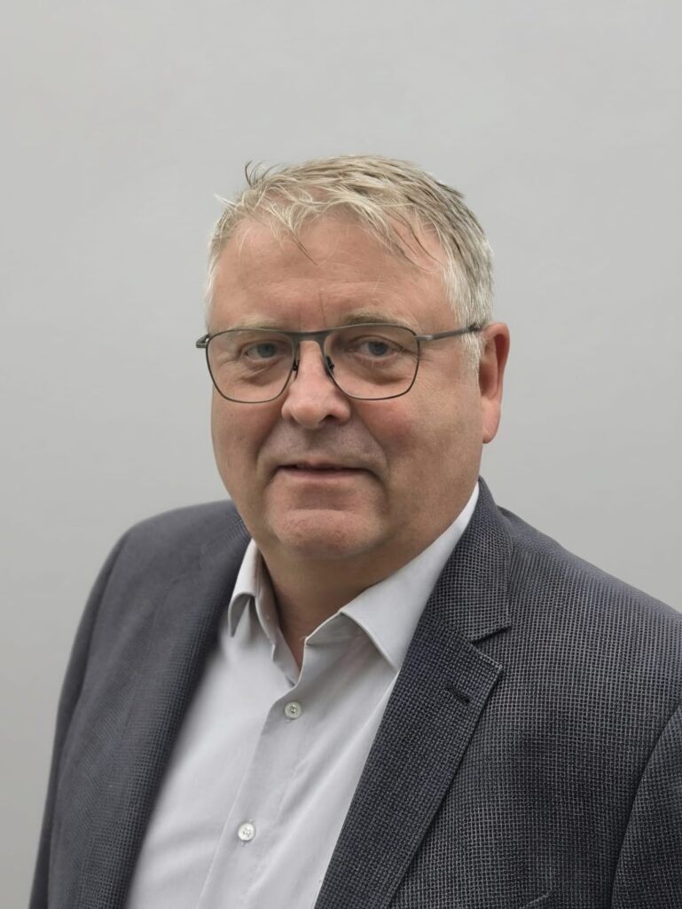 Älterer Mann mit neutralem Blick, grauem Anzug, Brille und silbernem Haar